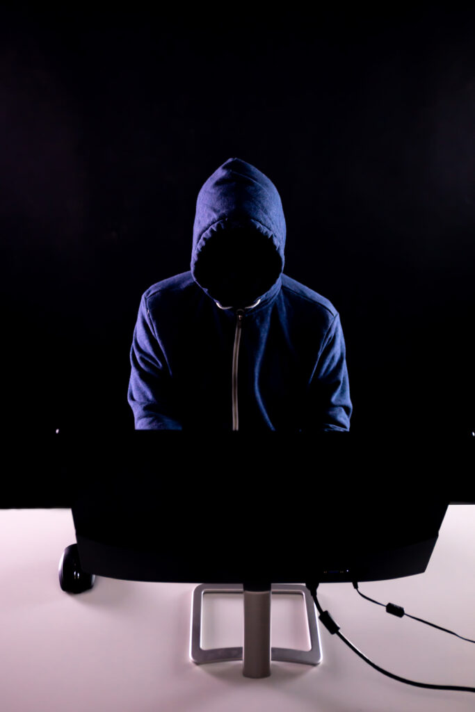 Anonymous and faceless hacker under hoodie using computer isolated over dark background - illegal online internet criminal concept