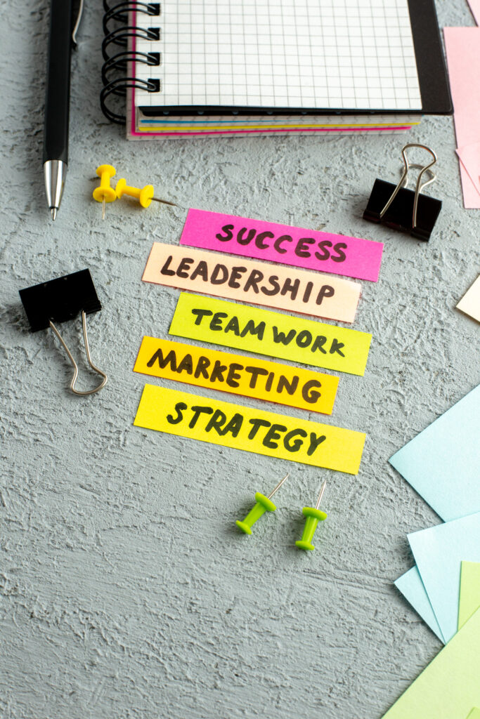 Front view of coloured envelopes and teamwork marketing strategy success leadership writings spiral notebook on gray sand background